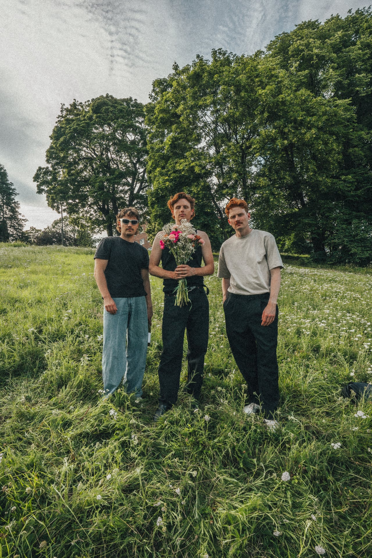 The three members of Daytrip standing in a wildflower field, one holding a bouquet